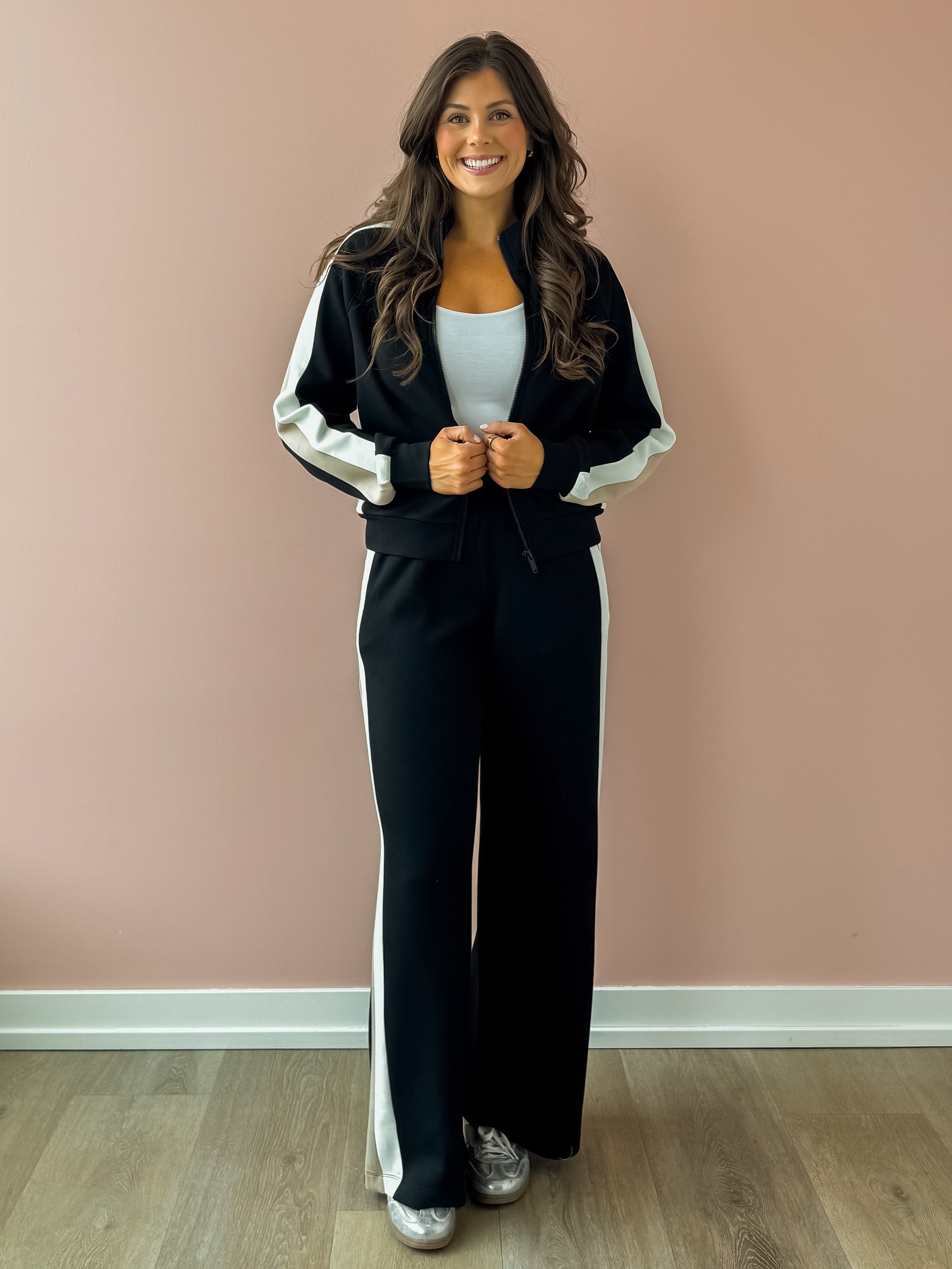 Woman wearing a black and white tracksuit against a pink wall