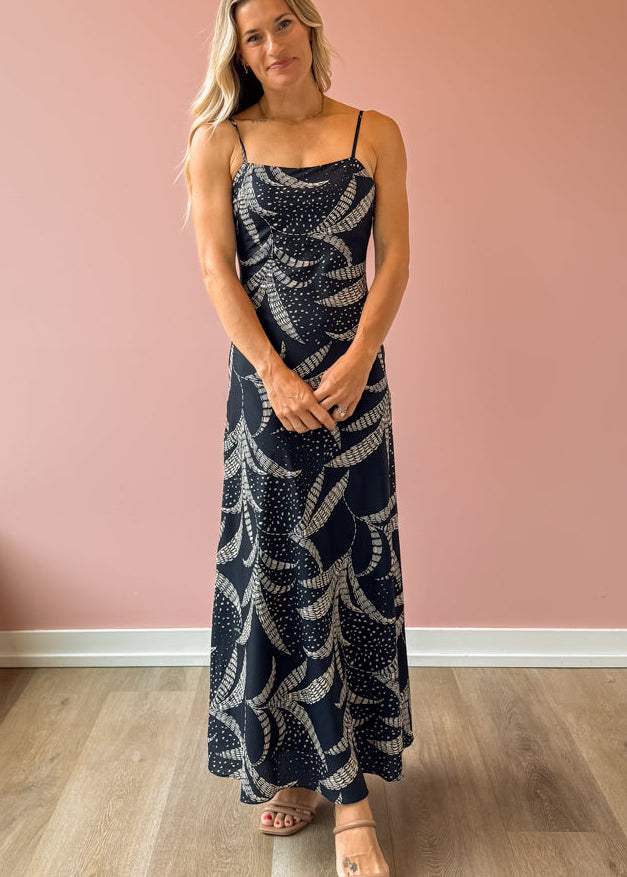 Woman wearing a navy blue dress with white patterns against a pink wall.