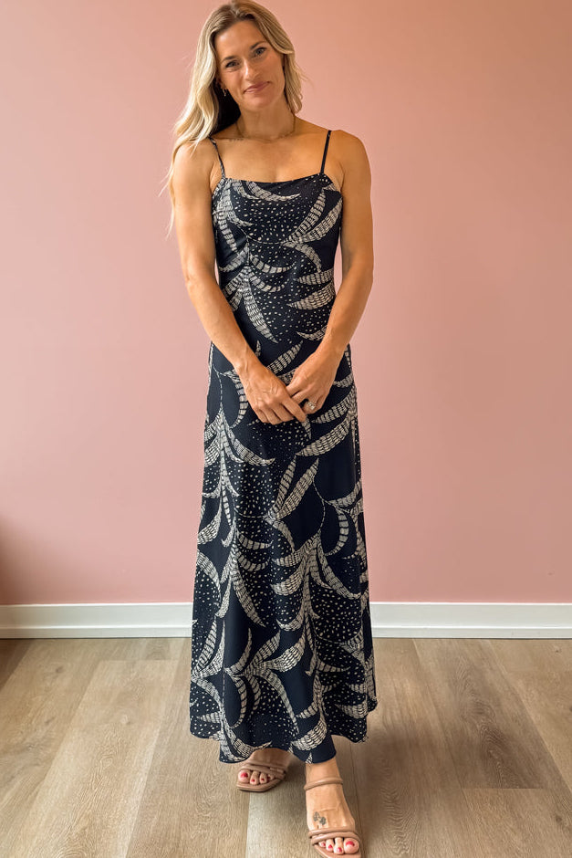Woman wearing a navy blue dress with white patterns against a pink wall.