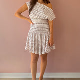 Woman wearing a white patterned dress against a pink wall