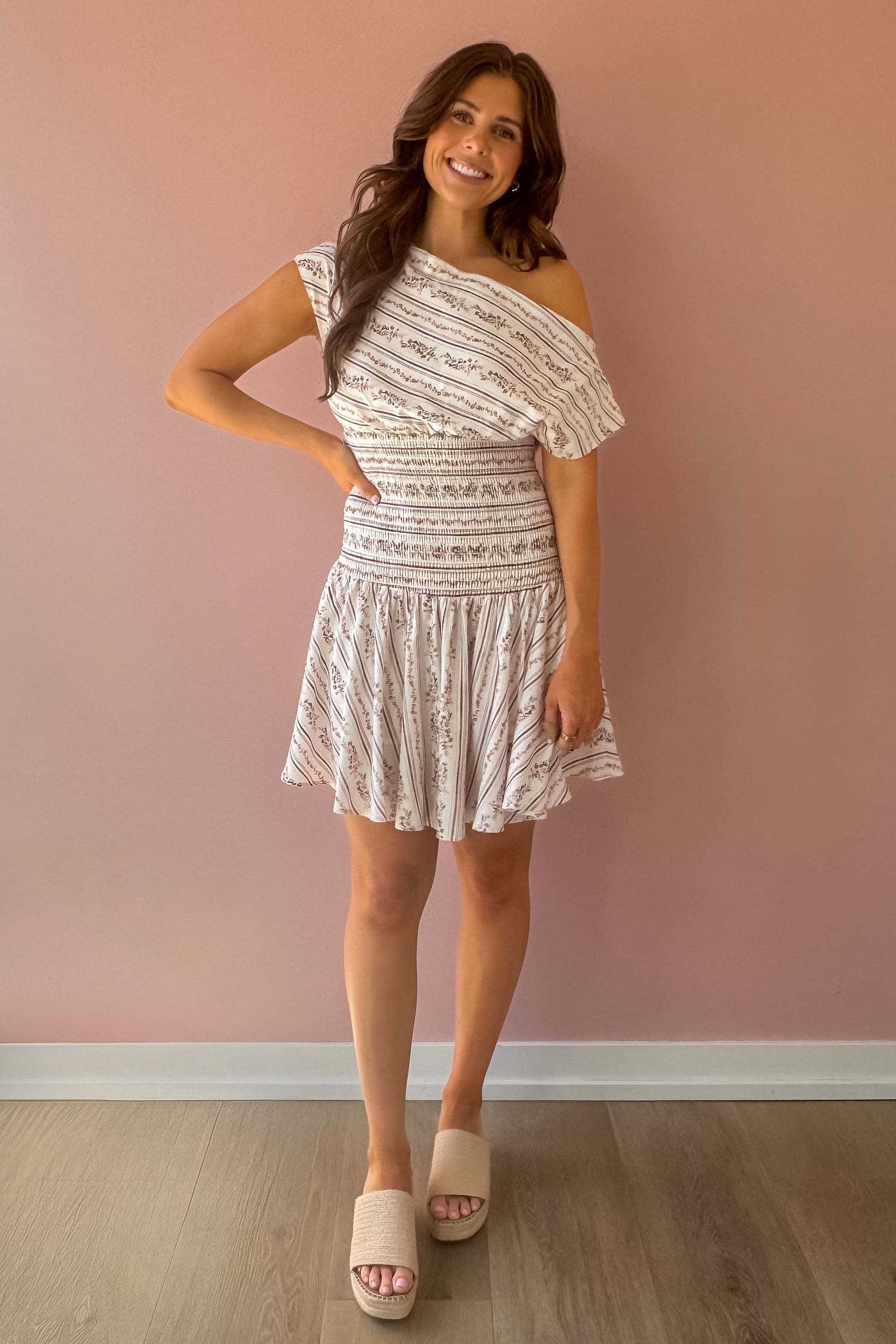 Woman wearing a white patterned dress against a pink wall
