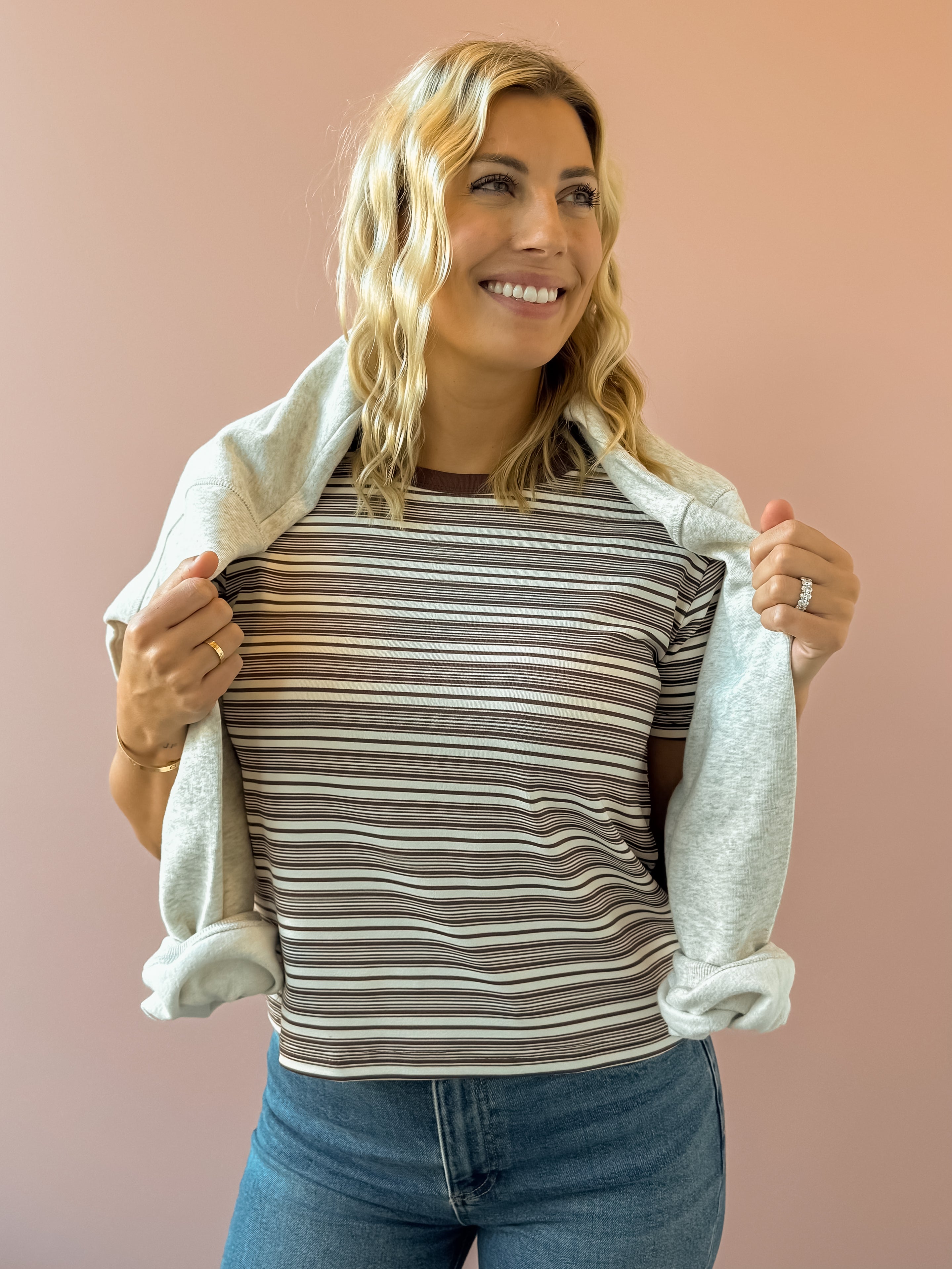 Olivaceous Mila Stripe Baby Tee in brown and white stripe, close-up front view, sweatshirt over shoulders.