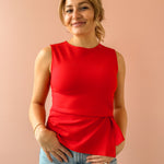 Woman wearing a red sleeveless top and blue jeans against a beige background
