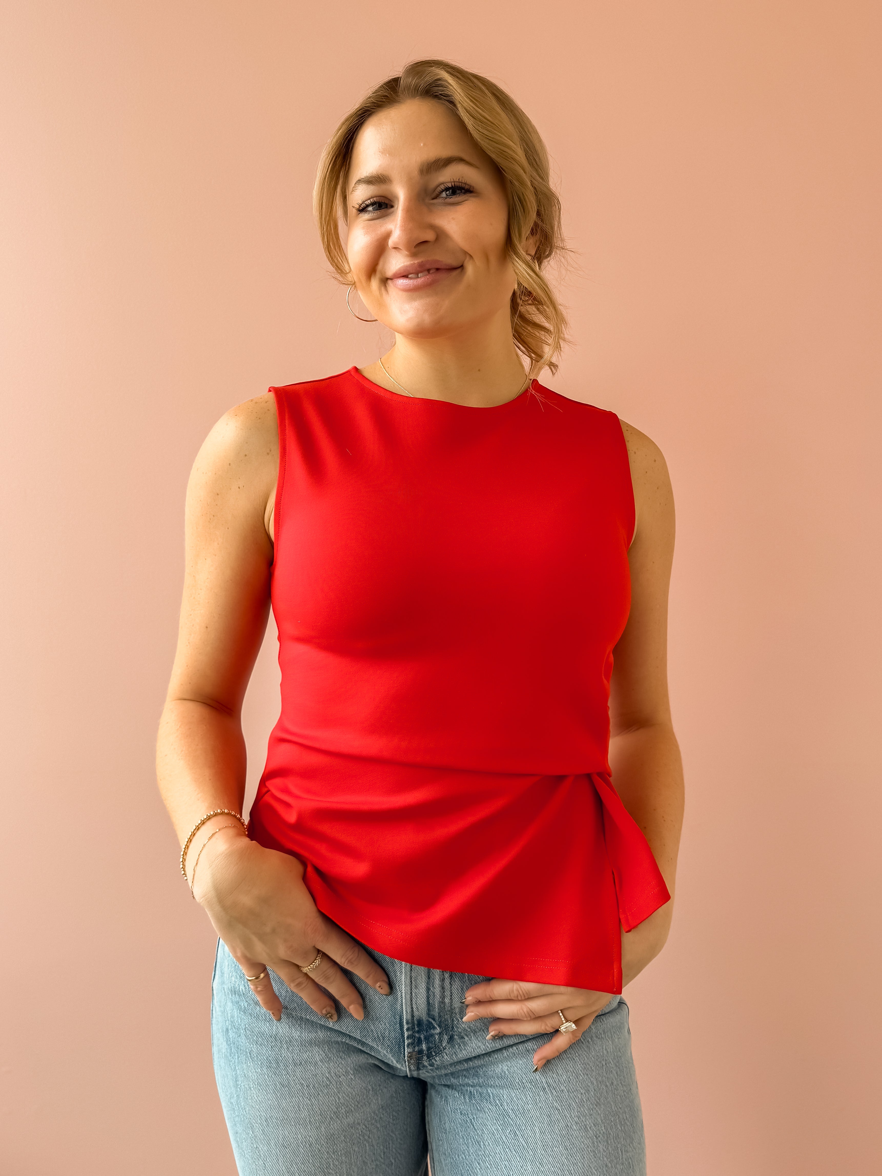 Woman wearing a red sleeveless top and blue jeans against a beige background
